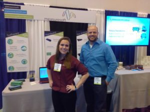 Two professionals posing near their table at a tradeshow